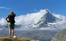 Person mit Rucksack blickt auf das Matterhorn in den Schweizer Alpen, umgeben von Wolken und Berglandschaft.