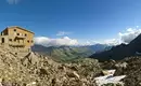 Alpenhütte umgeben von majestätischen Berggipfeln und sonniger Landschaft.