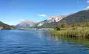 Blick auf alpinen See, umgeben von Bergen und blauer Himmel.