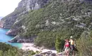 Zwei Wanderer auf einem felsigen Küstenpfad mit Blick auf das Meer und die rauen Felsen von Sardinien.