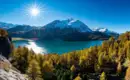 Bergpanorama mit schneebedeckten Gipfeln und blauem See im Engadin, herbstliche Bäume im Vordergrund.