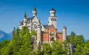 Blick auf Schloss Neuschwanstein inmitten von grünen Wäldern und blauen Himmel.