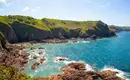 Klippenlandschaft auf Jersey, umgeben von blauem Meer und grünem Gras.