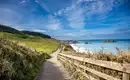 Küstenpfad in Irland mit blauem Himmel und Meer.