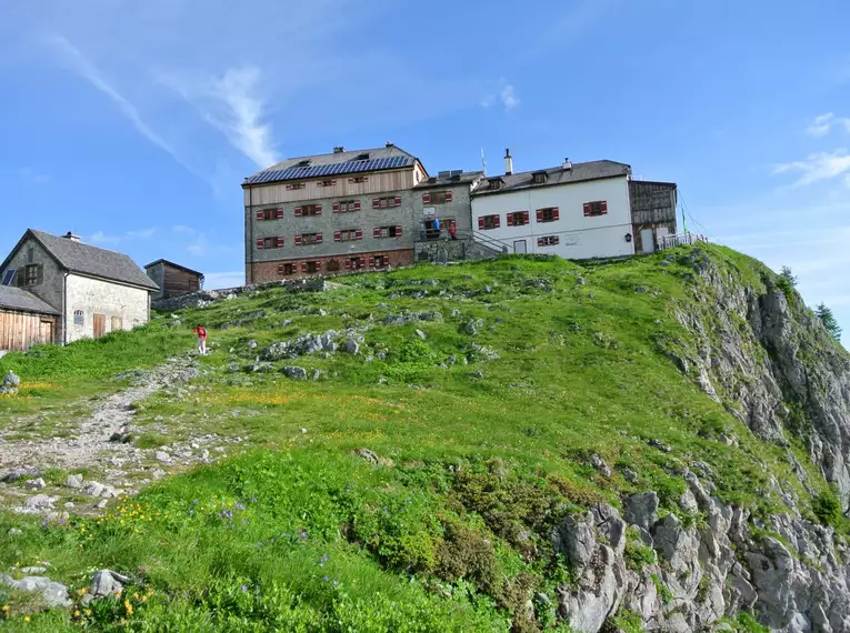 Das Watzmannhaus thront auf einem grünen Hügel mit Bergpanorama.