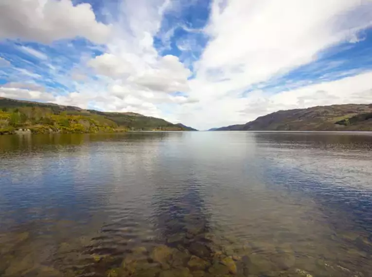 Weitläufiger schottischer See mit bewölktem Himmel und umgebenden Hügeln