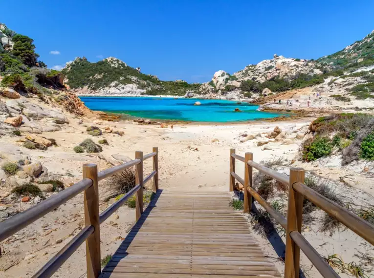 Holzsteg führt zur sandigen Bucht mit klarem, türkisfarbenem Wasser auf Sardinien.