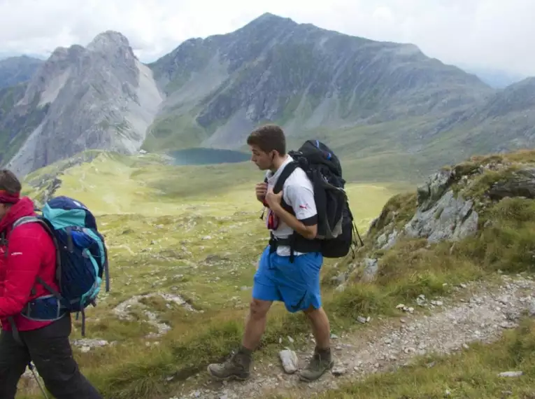 Zwei Wanderer mit Rucksäcken in den alpinen Landschaften Südtirols, Bergsee im Hintergrund.