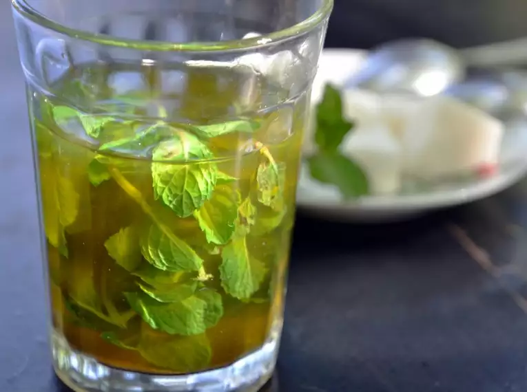 Ein Glas marokkanischer Minztee mit frischer Minze und Zucker im Hintergrund.