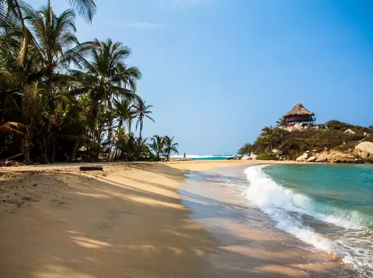 Ein idyllischer Sandstrand im Tayrona-Nationalpark mit türkisem Wasser und Palmen.