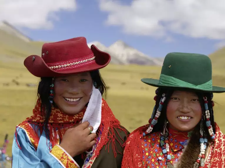 Zwei Frauen in traditioneller tibetischer Tracht vor Bergkulisse.