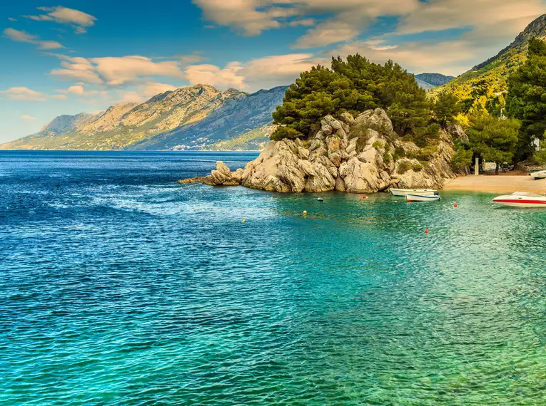 Szenische Aussicht auf das kristallklare Meerwasser, kleine Boote und majestätische Berge an der kroatischen Küste im Hintergrund.