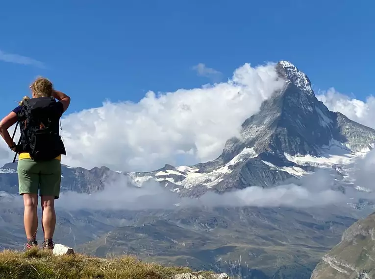 Person mit Rucksack blickt auf das Matterhorn in den Schweizer Alpen, umgeben von Wolken und Berglandschaft.