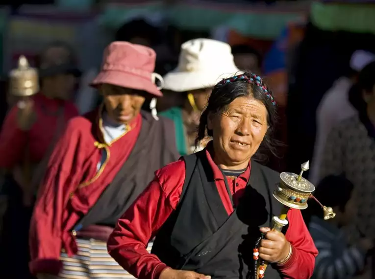 Menschen mit Gebetsmühlen in traditioneller tibetischer Kleidung auf einem Pilgerweg in Tibet.