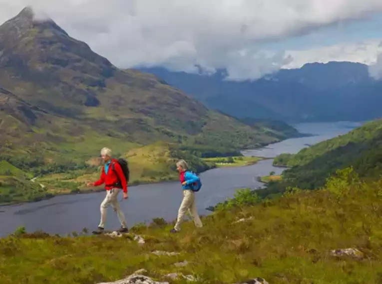 Zwei Personen wandern auf einem Hügel mit Blick auf Loch und Berge in Schottland.