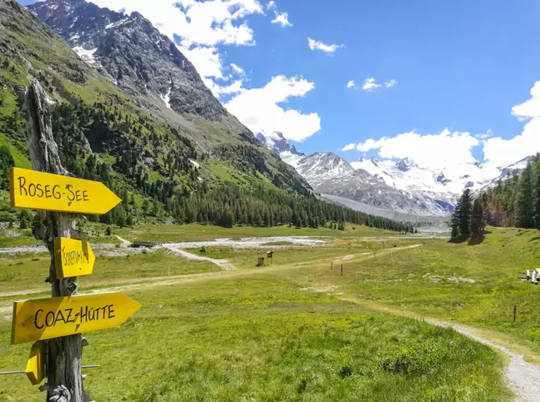 Wanderwegweiser im Rosegtal mit Blick auf die Schweizer Alpen.