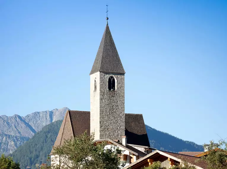 Kirchturm in Südtirol vor Alpenpanorama und blauem Himmel.