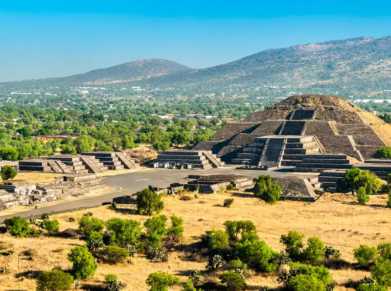 Panoramablick auf die antiken Pyramiden von Teotihuacán in Mexiko, umgeben von Bäumen und Bergen.