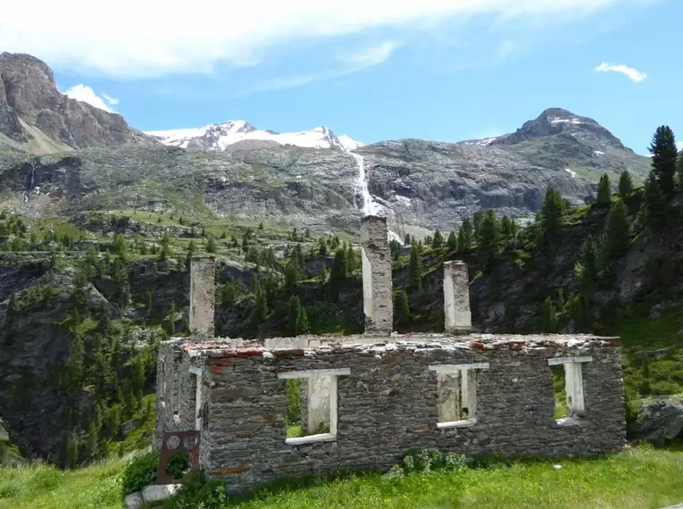 Alte Ruine vor malerischer Bergkulisse in Südtirol mit grünen Bäumen und schneebedeckten Gipfeln.