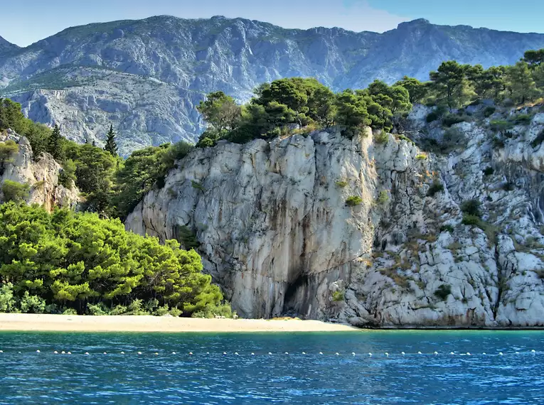 Küste mit grün bewachsenen Felsen und Bergblick in Kroatien