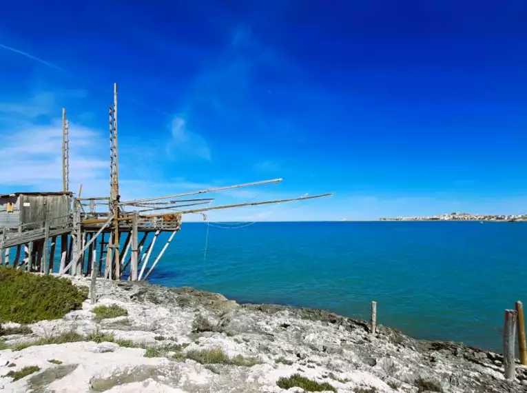 Ein Trabucco an der felsigen Küste von Apulien bei klarem Wetter.