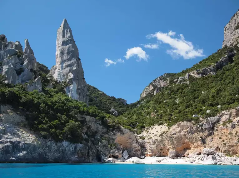 Felsige Küstenlandschaft mit klarem blauem Wasser und grüner Vegetation auf Sardinien.