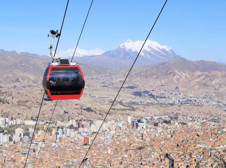 Rote Seilbahn fährt über das Stadtbild von La Paz mit Bergen im Hintergrund.