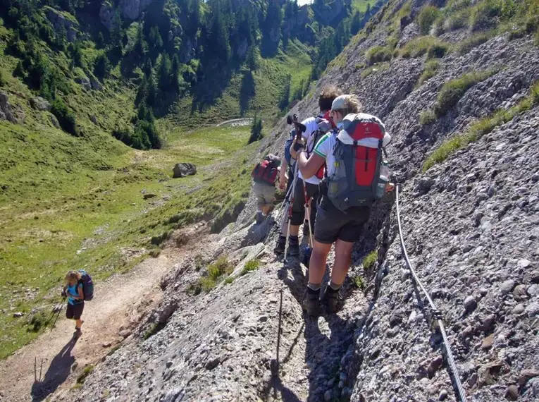 Gruppe von Wanderern auf schmalem Bergpfad in alpiner Landschaft.