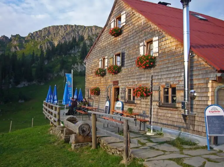 Eine rustikale Berghütte, Gundalpe, mit Blumen am Balkon, umgeben von Bergen.