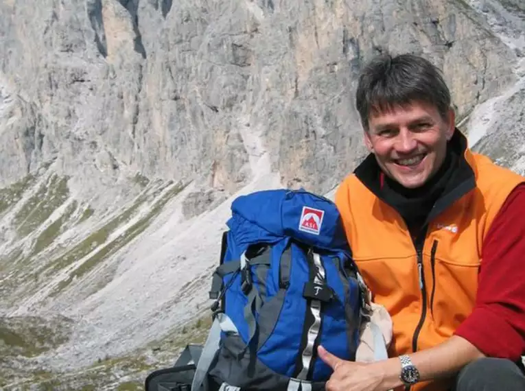 Ein Wanderer sitzt mit Rucksack vor einer steinigen Alpenlandschaft.