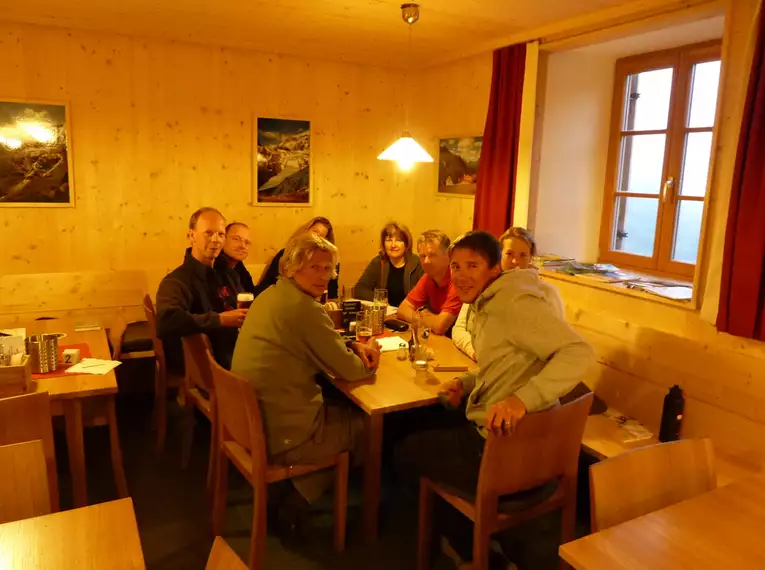 Eine Gruppe von Menschen sitzt an einem Holztisch in einer Berghütte.