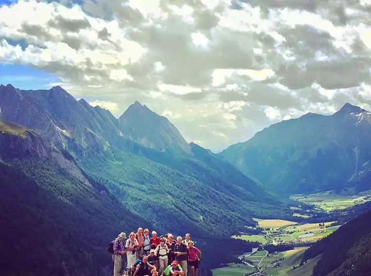 Gruppe von Wanderern auf einem Berg mit Alpentälern im Hintergrund.