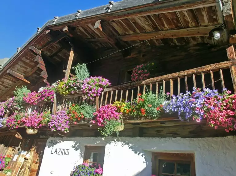 Altes Berghaus mit bunten Blumen an Balkonen in alpiner Umgebung.