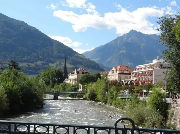 Fluss mit Brücke und Stadtansicht vor alpiner Kulisse in Meran