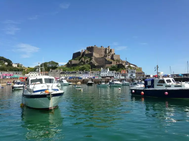 Boote im Hafen vor historischem Gebäude auf Jersey, sonniges Wetter.