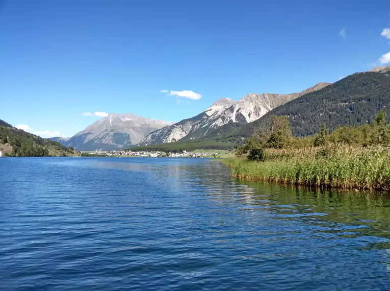 Blick auf alpinen See, umgeben von Bergen und blauer Himmel.