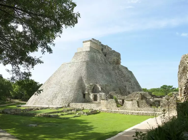 Steinerne Pyramide von Uxmal in einer grünen Landschaft, unter einem klaren blauen Himmel.