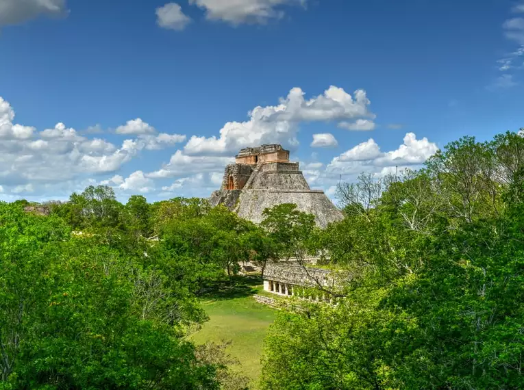 Die beeindruckenden Maya-Ruinen von Uxmal, umgeben von dichtem Grün, unter einem strahlend blauen Himmel.