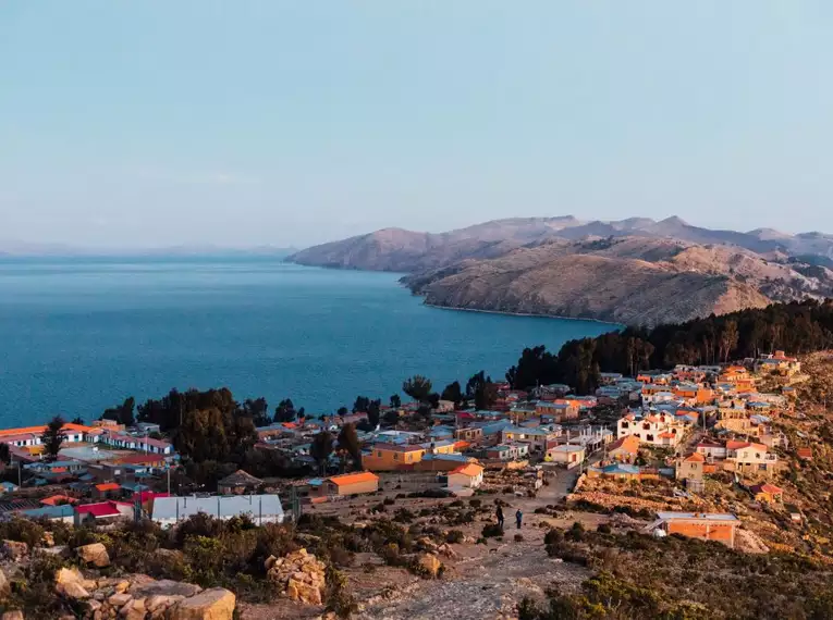 Panoramablick auf ein Dorf auf der Isla del Sol am Titicacasee, umgeben von Hügeln unter klarem Himmel.