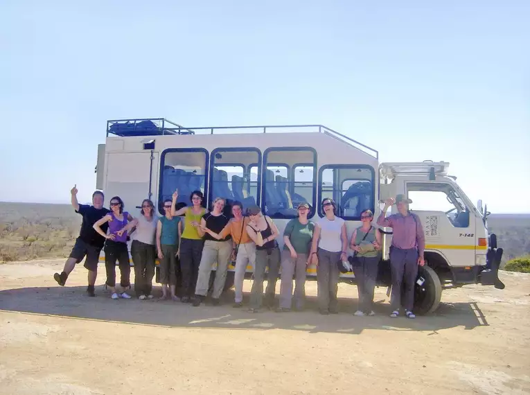 Eine Reisegruppe steht vor einem Safari-Fahrzeug in Südafrika.