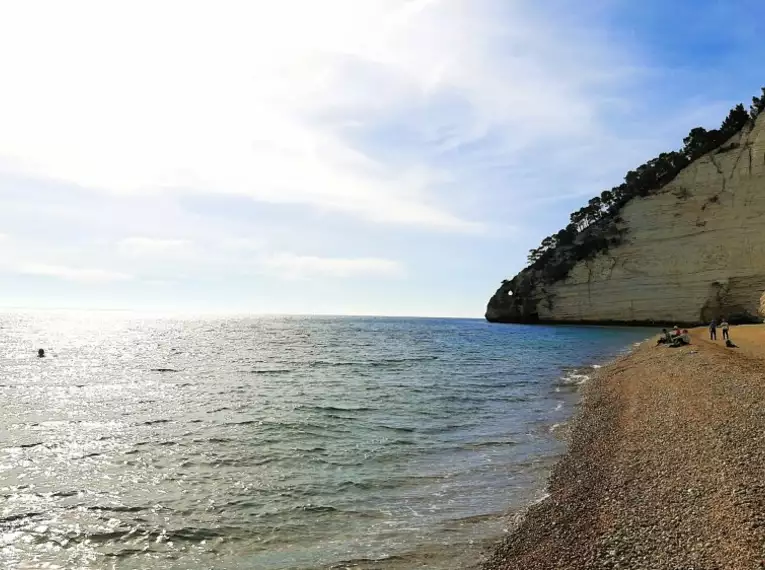 Blick auf die Küste Apuliens mit steiler Felswand und Kiesstrand am Meer.