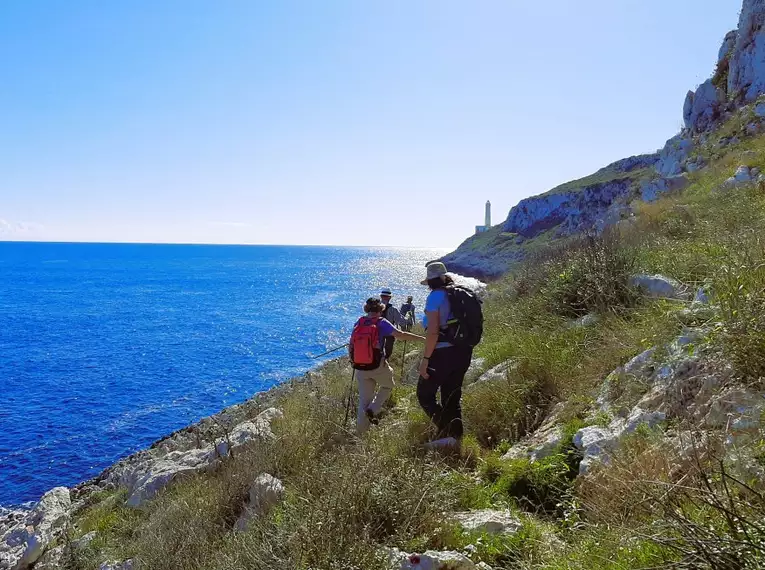 Wanderer auf einem felsigen Küstenpfad mit Blick auf das blaue Meer unter klarem Himmel.