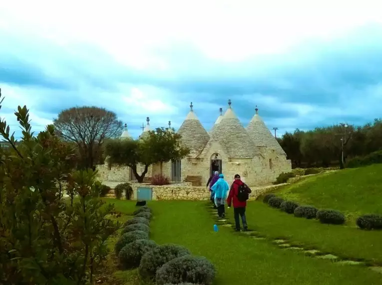 Menschen besuchen Trulli-Häuser in einer grünen Landschaft, Apulien.