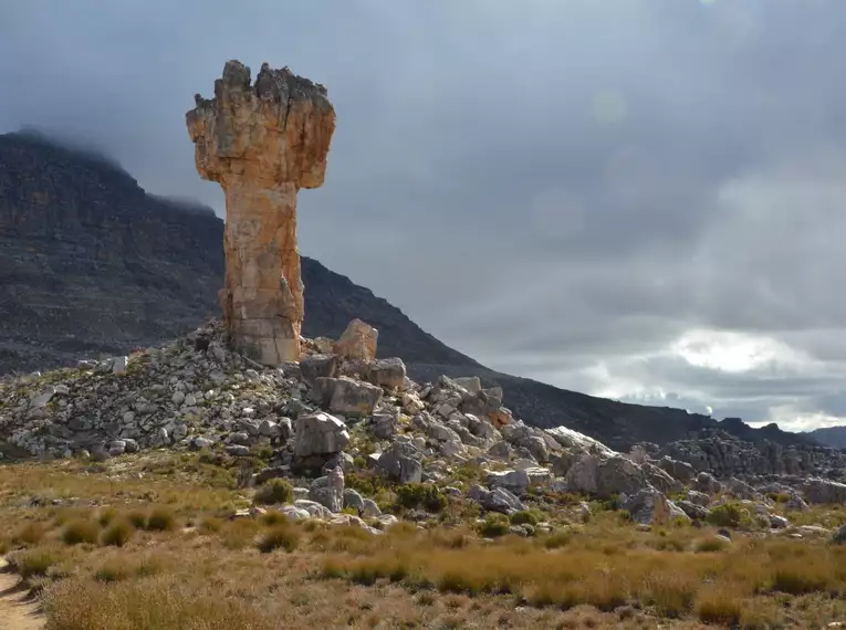 Felsenformation in den Cederbergen, umgeben von Bergen und bewölktem Himmel.