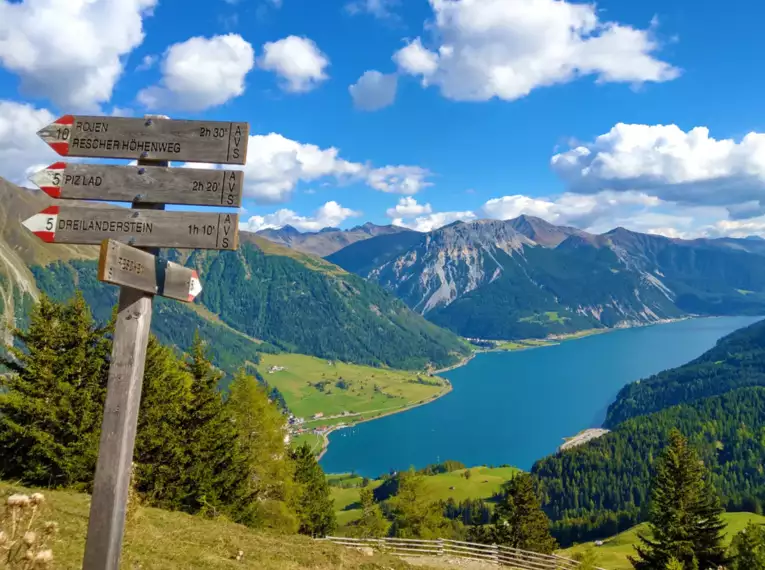 Wanderwegweiser mit Blick auf den Reschensee in den Alpen.