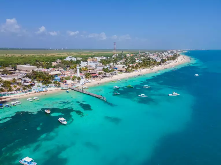 Küstenlinie von Puerto Morelos mit Booten im Wasser und blauem Himmel.