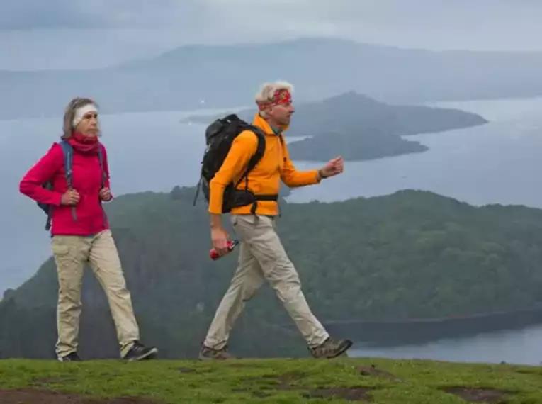 Zwei Personen wandern mit Rucksäcken am Loch Lomond in Schottland.