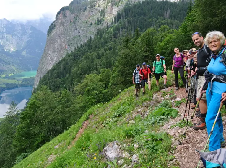 Eine Wandergruppe auf einem Bergpfad mit Blick auf den Königssee und bewaldete Hänge.