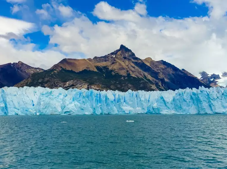 Blau schimmernder Gletscher vor steilem Berg unter blauem Himmel in Patagonien.