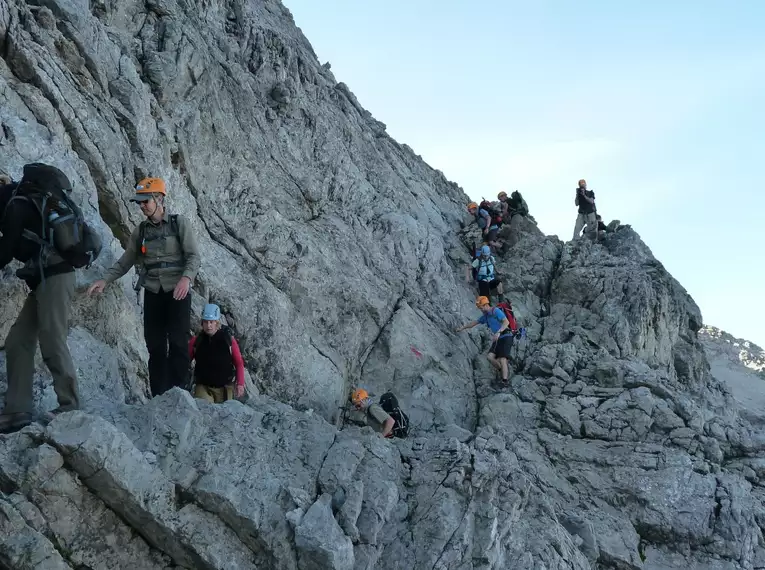 Gruppe von Bergwanderern erklimmt felsigen Grat im Allgäu, gesichert mit Helmen.